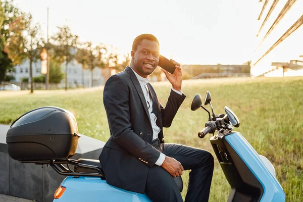 Positivo nero uomo d'affari con scooter utilizzando il suo telefono — Foto Stock