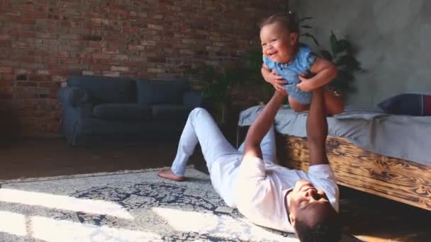 African dad lying on beautiful carpet in modern bedroom play with daughter. — Stockvideo