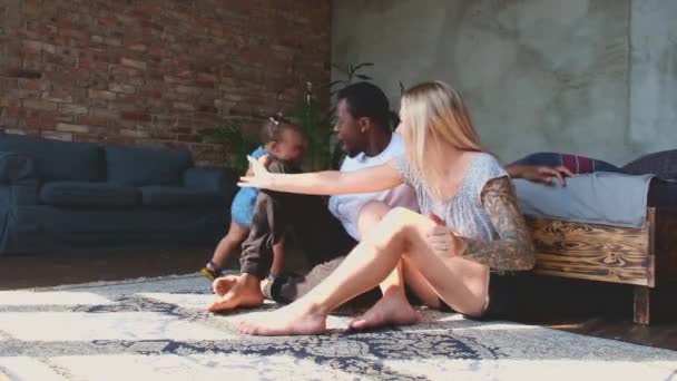 Niña africana aprendiendo a caminar en casa mientras los padres se sientan en el piso en el estudio. — Vídeo de stock