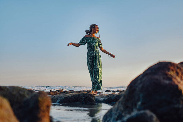 Shot of woman weared in green dress walking on beach alone in bali at sunset.