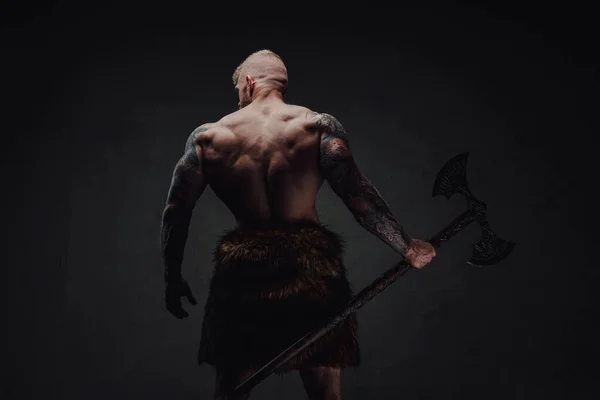 Visão traseira de guerreiro tatuado saudável na pele com machado em um fundo escuro — Fotografia de Stock