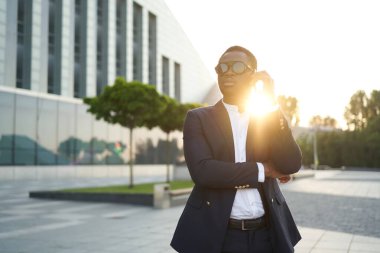 Afrikalı iş adamı şehir manzarasına karşı telefonda konuşuyor.
