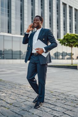 Bilgisayarlı başarılı bir iş adamı dışarıda telefonla konuşuyor.