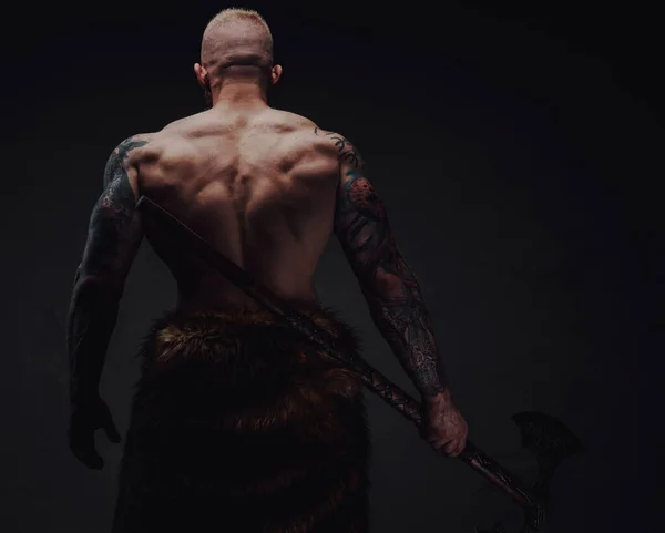 Οπίσθια όψη υγιούς πολεμιστή με τατουάζ σε γούνα με τσεκούρι σε σκούρο φόντο — Φωτογραφία Αρχείου