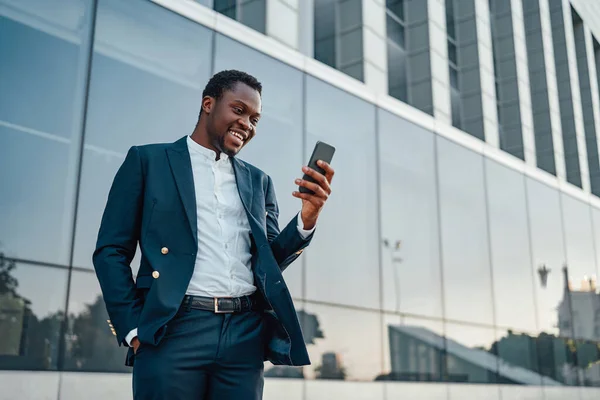 Оптимистичный черный руководитель, использующий свой телефон против здания — стоковое фото