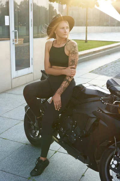 Mulher adulta elegante com chapéu posando na motocicleta urbana — Fotografia de Stock