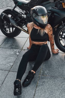Şehir caddesinde siyah motosikletli dövmeli bir kadın motorcu.