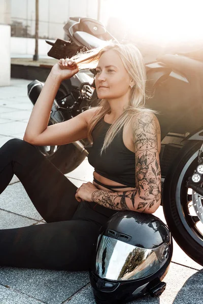 Mulher desportiva motociclista com motocicleta preta no asfalto — Fotografia de Stock