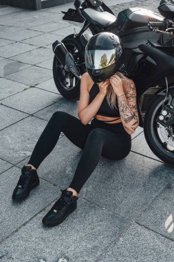 Şehir caddesinde siyah kasklı ve motosikletli bir kadın.