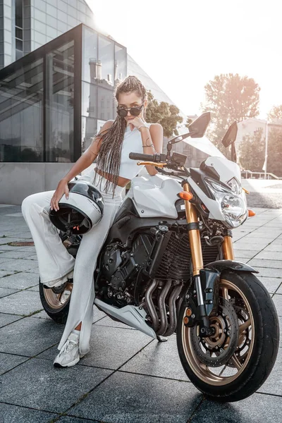 Женщина в мотоциклетном шлеме опирается на мотоцикл на тротуаре — стоковое фото