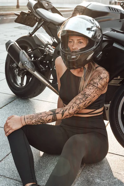 Γυναίκα μοτοσικλετιστής με μαύρη μοτοσικλέτα ποζάρουν έξω στην πόλη — Φωτογραφία Αρχείου