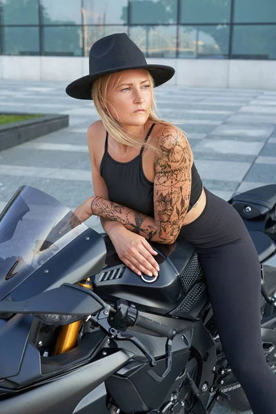 Модна доросла жінка з капелюхом позує на міському мотоциклі — стокове фото