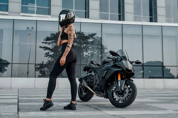 Женщина, одетая в черную спортивную одежду и мотоцикл снаружи — стоковое фото