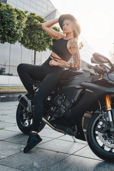 Žena motorkář s kloboukem pózování nakloněný moderní motocykl — Stock fotografie
