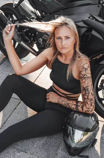 Sportiv kvinna biker med svart motorcykel på asfalt — Stockfoto