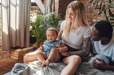 Neşeli anne ve baba, yeni yürümeye başlayan çocukları yatakta dinleniyor.