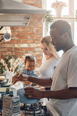 Ailesi mutfakta yemek pişirirken neşeli küçük bir kız.