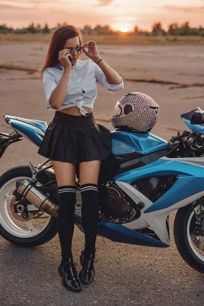 Stylová žena nosí sluneční brýle nakloněný motocykl při západu slunce — Stock fotografie