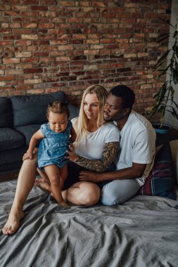 Multiethnic parents teaching their daughter to walk on bed