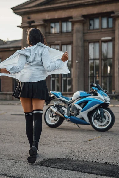 Woman undressing her shirt against motorcycle and building