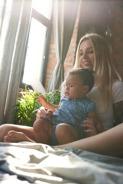 Mother embracing her daughter sitting on bed in daytime — Stock Photo, Image