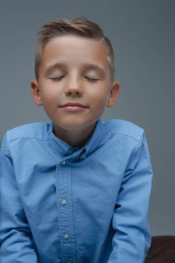 Kapalı gözlü küçük çocuk gri arka planda rahatlıyor.