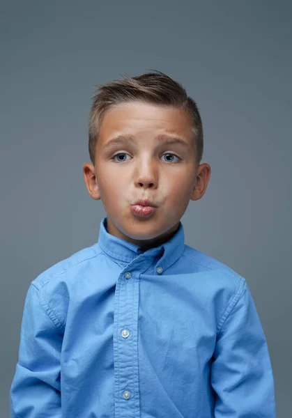 Garçon ludique faisant visage et posant sur fond gris — Photo