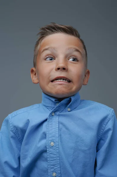 Playful boy making face and posing against grey background — Stock Photo, Image