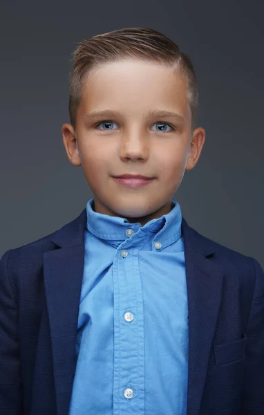 Kleine jongen gekleed in kostuum poseren tegen grijze achtergrond — Stockfoto