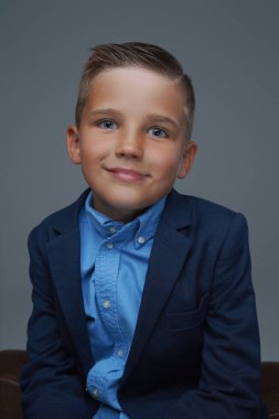 Takım elbiseli neşeli çocuk gri arka planda poz veriyor.