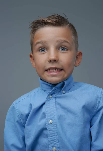Lekfull pojke gör ansikte och poserar mot grå bakgrund — Stockfoto
