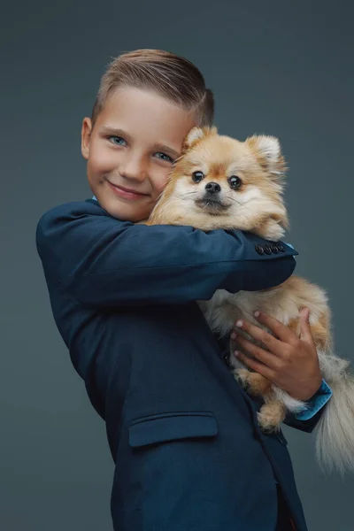 Щасливий хлопчик з крихітною собачкою на сірому фоні — стокове фото