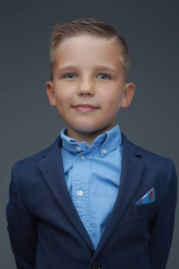 Gri arka planda poz veren kostüm giymiş küçük bir çocuk.