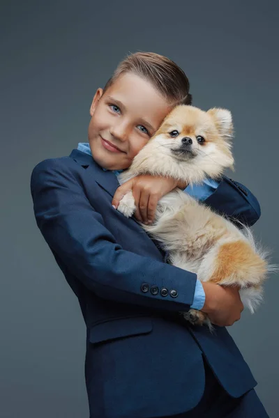 Щасливий хлопчик з крихітною собачкою на сірому фоні — стокове фото
