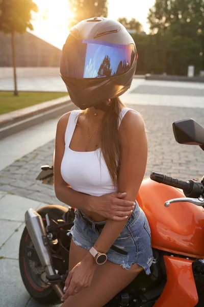 Slim motociclista feminino com capacete posando em torno de bicicleta fora — Fotografia de Stock