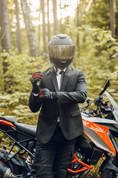 Bonito motociclista com capacete e motocicleta escura na floresta — Fotografia de Stock