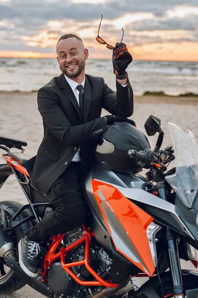 Gioioso motociclista in giacca e cravatta in sella alla moto sportiva sulla spiaggia — Foto Stock