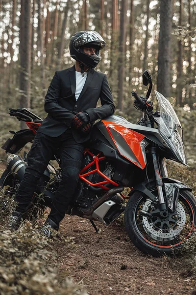 Uomo indossato in tuta nera con moto scura nella foresta — Foto Stock