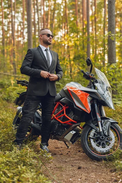 Όμορφος άνδρας με κοστούμι με σκούρα μοτοσικλέτα στο δάσος — Φωτογραφία Αρχείου