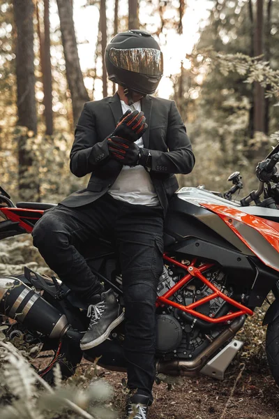 Uomo d'affari motociclista con guanti e casco in posa nella foresta — Foto Stock