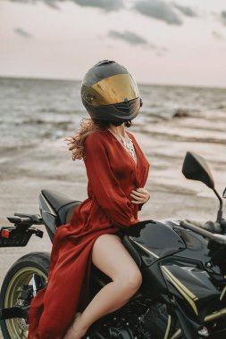 Bisikletle denize karşı poz veren kasklı zayıf kadın motorcu.