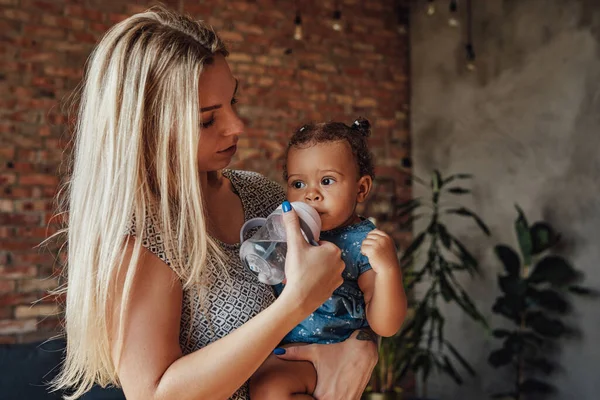Blonde Mutter füttert ihre kleine Tochter zu Hause — Stockfoto