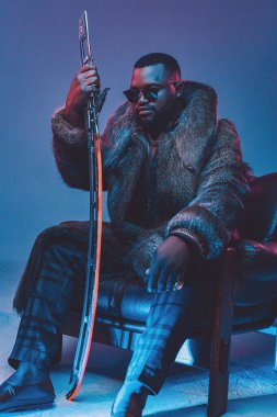 Deri koltukta oturan kılıçlı Afrikalı adam.