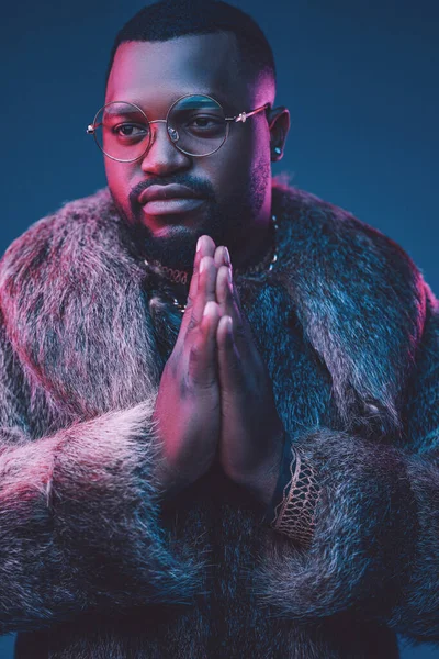 Praying african man with fur coat against dark background — Stock Photo, Image