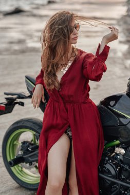 Sahilde siyah motosikletle rahatlayan baştan çıkarıcı bir kadın.