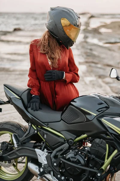 Мотоциклистка со шлемом, позирующая вокруг велосипеда на пляже — стоковое фото