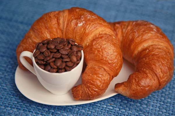 Zwei Croissants und Kaffeebohnen in einer winzigen Tasse — Stockfoto