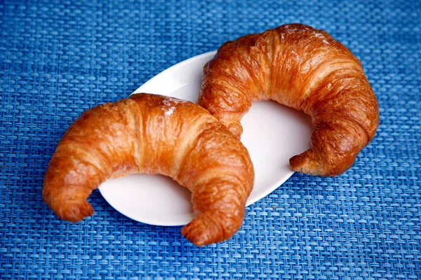 Due croissant su un piatto bianco con sfondo blu — Foto Stock