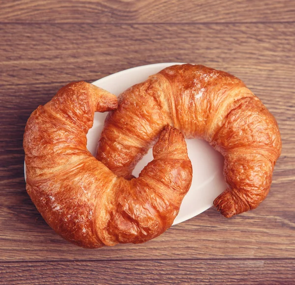 Dos croissants en un plato con fondo de madera —  Fotos de Stock