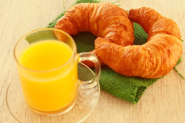 Two croissants on a green napkin and a mug of juice — Stock Photo, Image